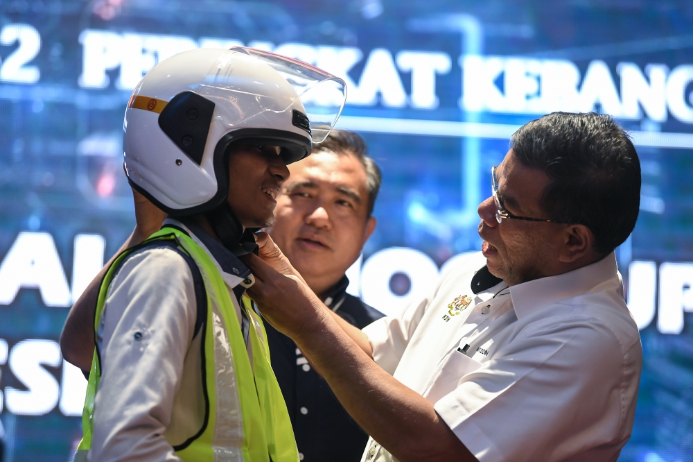 Home Minister Datuk Seri Saifuddin Nasution Ismail (right) helps fasten Muhammad Juwaidi Juslan’s helmet as Transport Minister Anthony Loke looks on during the launch of the MyLesen B2 national programme for motorcyclists in Sungai Petani May 30, 2023. — Bernama pic