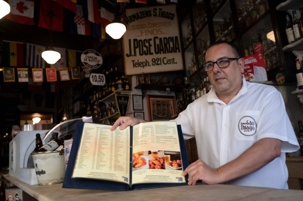 Carlos Fionda, 59, manager of Amazem Sao Thiago bar, shows their physical menu at the Lapa neighborhood in Rio de Janeiro, Brazil, on May 24, 2023. — AFP pic