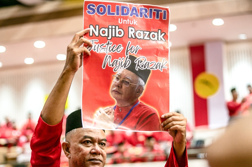 An Umno party member holds a ‘Solidarity for Najib Razak’ poster during the party’s 2023 general assembly at the World Trade Centre in Kuala Lumpur June 9, 2023. — Picture by Hari Anggara 