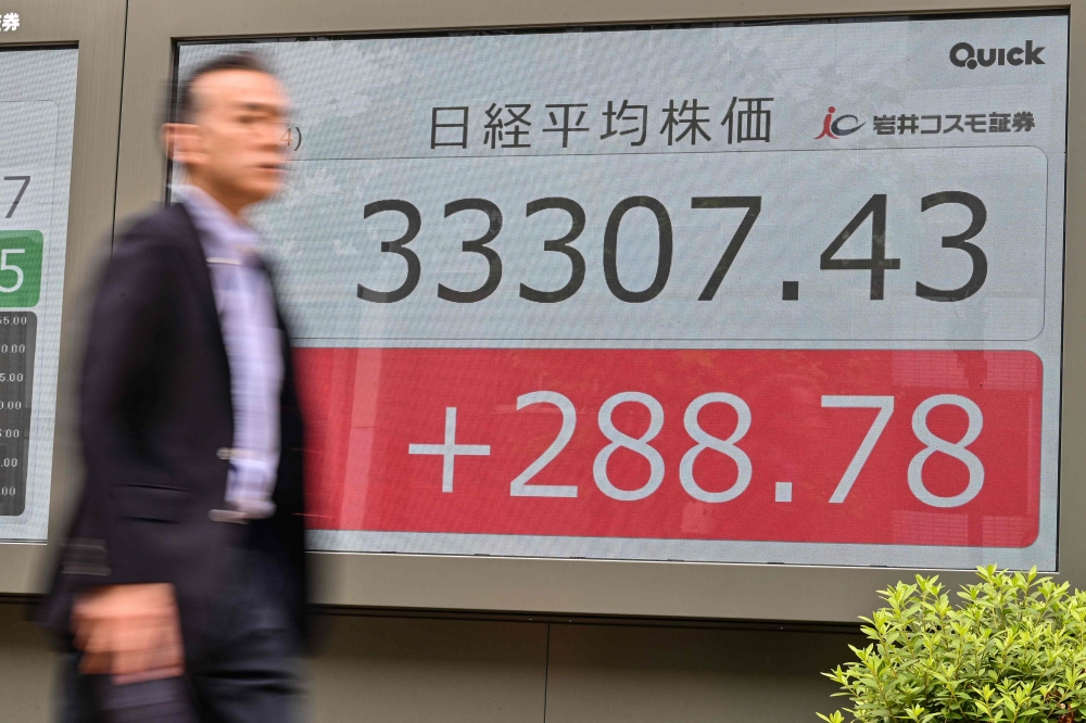 A man walks past an electronic board showing the numbers on the Tokyo Stock Exchange after the morning trading session ended, along a street in Tokyo June 14, 2023. — AFP pic