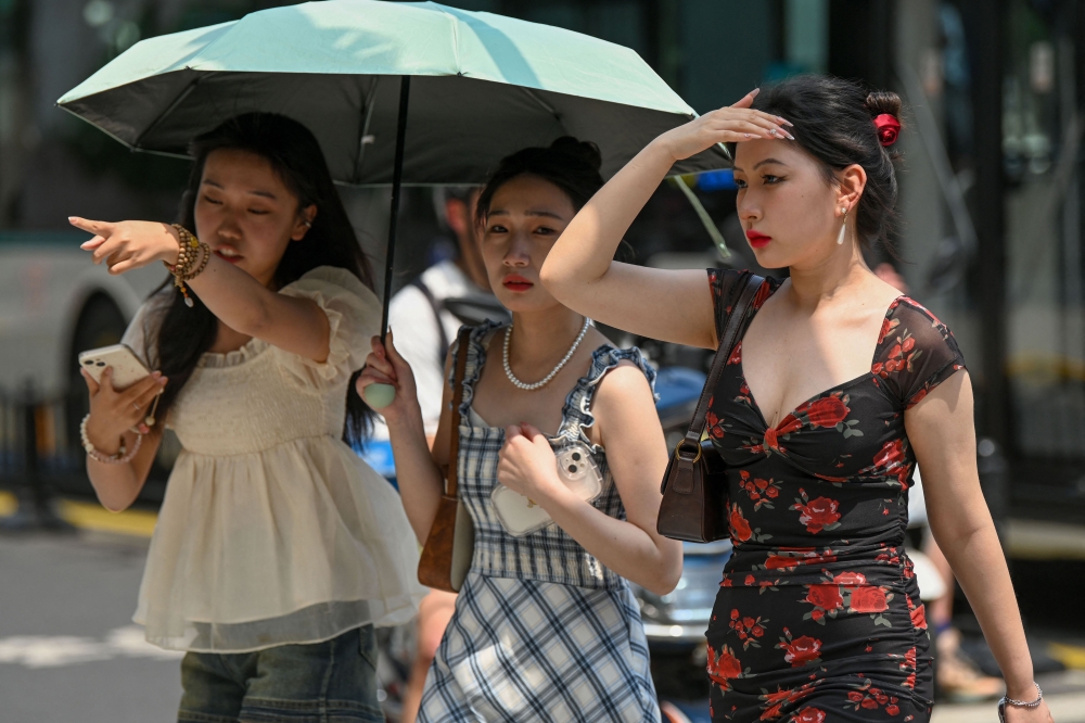 Women use an umbrella to shelter from the sun amid hot weather in Shanghai on May 29, 2023. — AFP pic