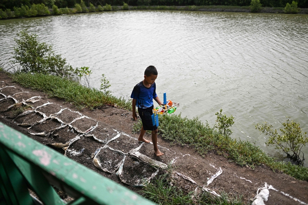 This photograph taken on June 14, 2023 shows Peeraphab Butrthong, one of the four pupils attending a school, carrying his science project, a solar-powered boat along the banks in Ban Khun Samut Chin, a coastal village less than 10km from the edge of Bangkok. — AFP pic 