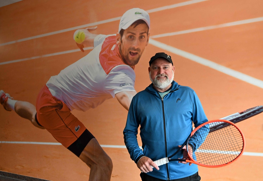 Jurulatih tenis Wolfgang Reiner bergambar di hadapan gambar besar pemain tenis Serbia Novak Djokovic di pusat tenis di Oberschleissheim dekat Munich, selatan Jerman, pada 23 Jun, 2023. — Gambar AFP