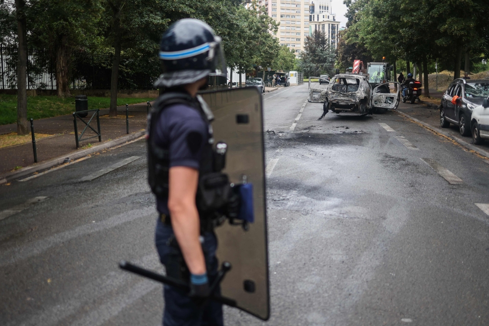 A French police officer in riot gear looks on next to burnt cars at the Pablo Picasso neighbourhood in Nanterre on July 1, 2023, after a fourth consecutive night of rioting in France over the killing of a teenager by police. — AFP pic