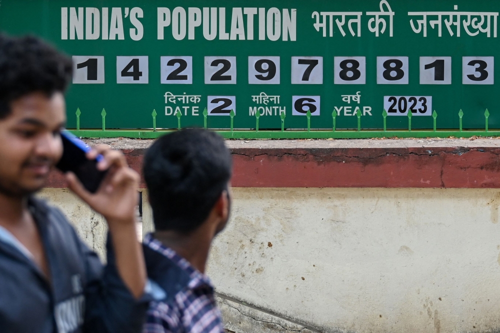 Pedestrians walk past a population clock board displayed outside the International Institute for Population Sciences (IIPS) in Mumbai on June 2, 2023. — AFP pic