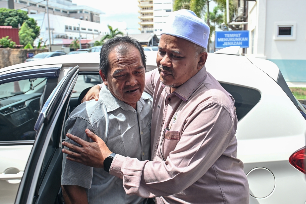 Eiyi Johari, 60, being comforted by exco Ariffin Deraman (right) at the Forensic Medicine Department of Sultanah Nur Zahirah Hospital, July 3, 2023. — Bernama pic 