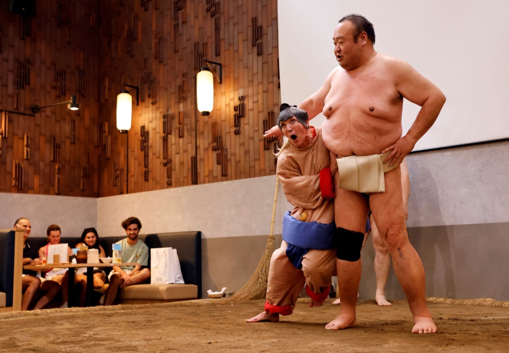 Nadine, seorang pelancong berusia 43 tahun dari AS, memakai kostum ahli gusti sumo, cuba bertanding melawan bekas ahli gusti sumo Towanoyama di gelanggang sumo sebelum pelancong dari luar negara, di Yokozuna Tonkatsu Dosukoi Tanaka di Tokyo, Jepun 30 Jun 2023. — Gambar Reuters