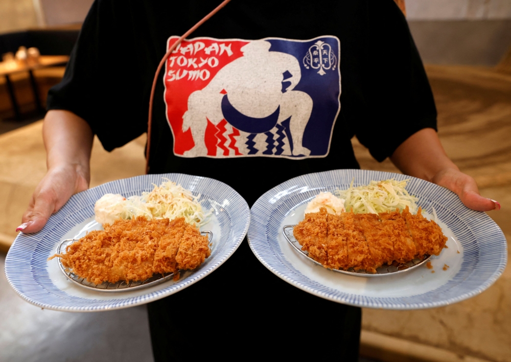 Seorang pekerja Yokozuna Tonkatsu Dosukoi Tanaka, sebuah restoran bertema gusti sumo, menghidangkan Tonkatsu atau potongan daging babi yang dilapisi tepung roti kepada pelancong dari luar negara, di Tokyo, Jepun 30 Jun 2023. — Gambar Reuters