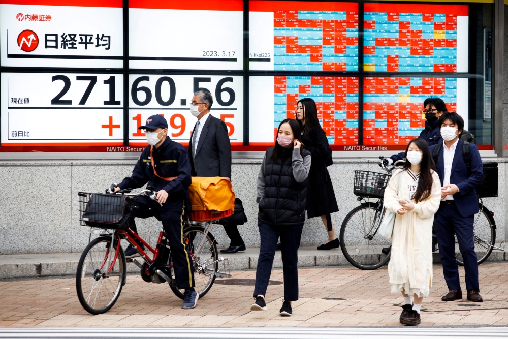 Passersby wait at a crossing in front of an electronic board showing Japan's Nikkei average outside a brokerage, in Tokyo March 17, 2023. — Reuters pic