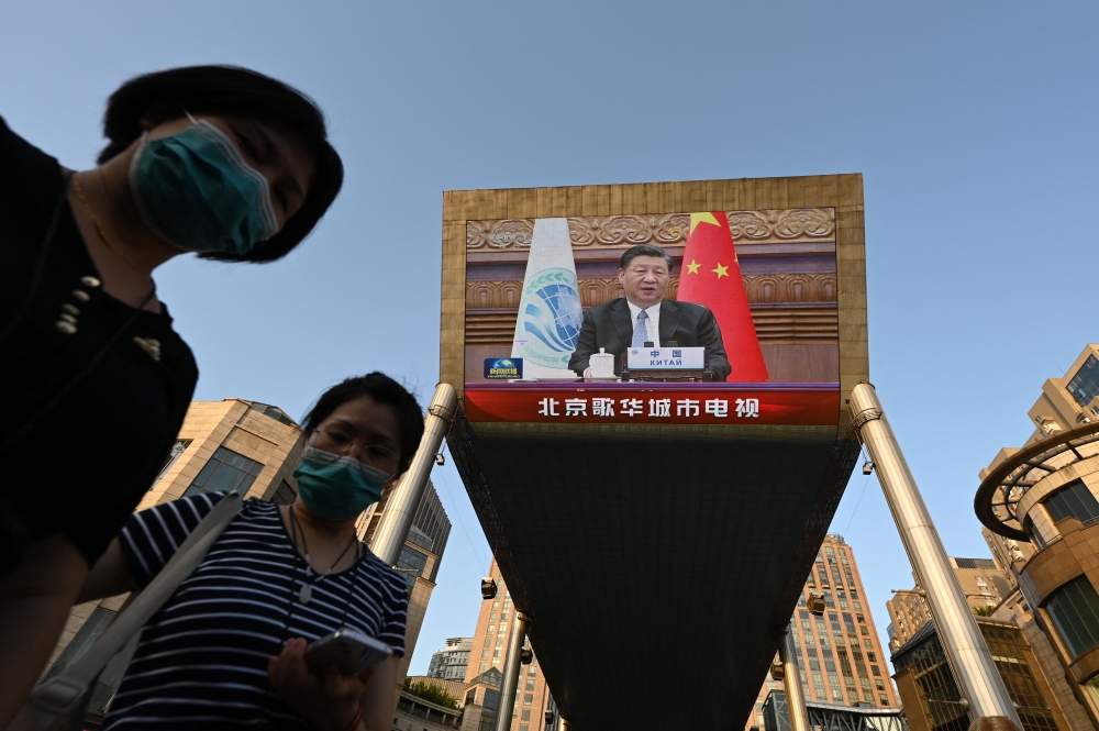Two women wait below a giant screen showing news footage of China's President Xi Jinping speaking virtually to the Shanghai Cooperation Organisation meeting, which was being held in India, at a shopping mall in Beijing on July 4, 2023. — AFP pic