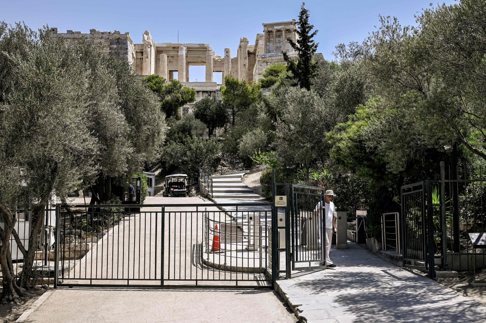 An employee closes the access gate to the Acropolis archaeological site in Athens on July 14, 2023. — AFP pic