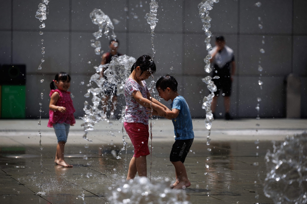 Children play as they cool off at a water fountain during a heat wave in Hong Kong on July 9, 2023. — AFP pic
