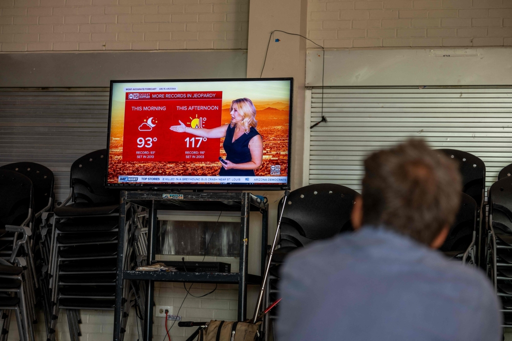A person seeking shelter from the heat watches the weather forecast at the First Congregational United Church of Christ cooling center on July 14, 2023 in Phoenix, Arizona. — AFP pic