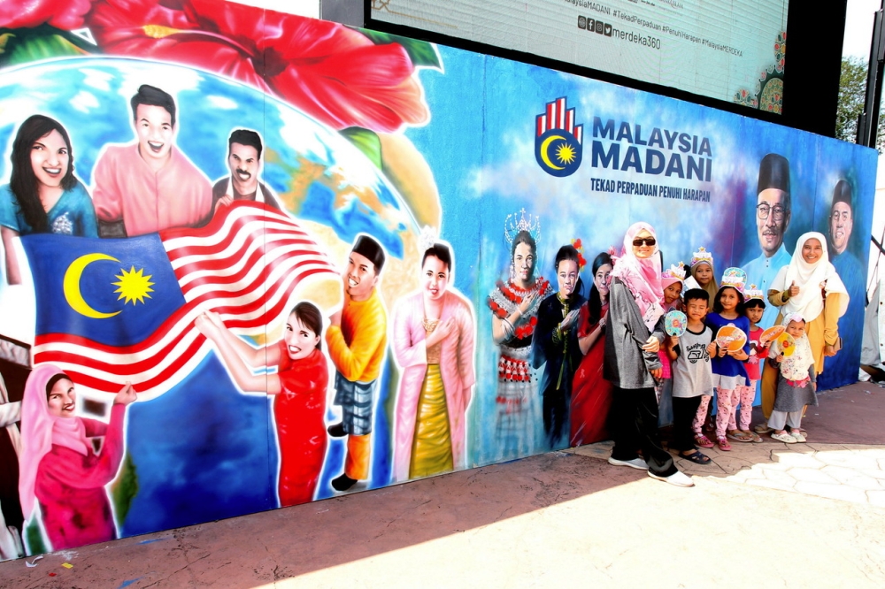 Juwariyah Sulaiman (right) from Taman Meru with her family poses in front of the Madani Malaysia Wall mural at the site of the 2023 National Month and Jalur Gemilang Waving ceremony at Sultan Azlan Shah Circle, Meru Raya, in Ipoh, July 15, 2023. — Bernama pic