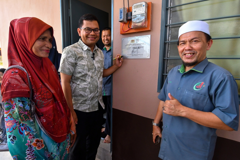 Local Government Development Deputy Minister Akmal Nasrullah Mohd Nasir (2nd left) signs a plaque while handing over a Urban Poverty Eradication Programme house to the family of Zaini Abdullah (left) in Kampung Tanjung Baru on Jalan Pantai Cahaya Bulan, Kota Baru July 16, 2023. — Bernama pic