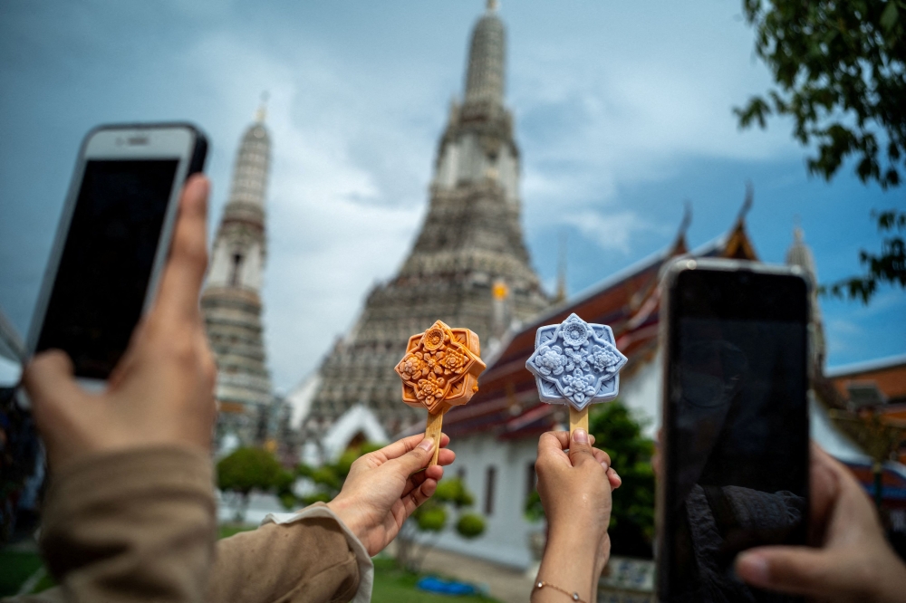 People take pictures of ice cream shaped like tiles of the famous Wat Arun temple, or Temple of Dawn, in Bangkok, Thailand July 8, 2023. — Reuters pic