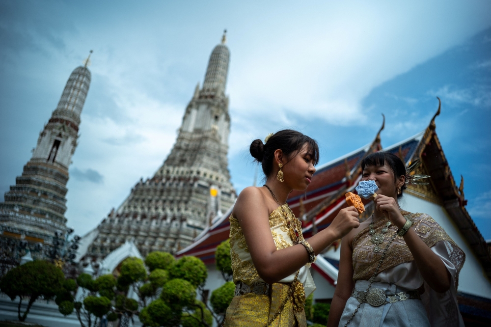 Women dressed in traditional Thai costumes eat ice creams shaped like tiles of the famous Wat Arun temple, or Temple of Dawn, in Bangkok July 8, 2023. — Reuters pic