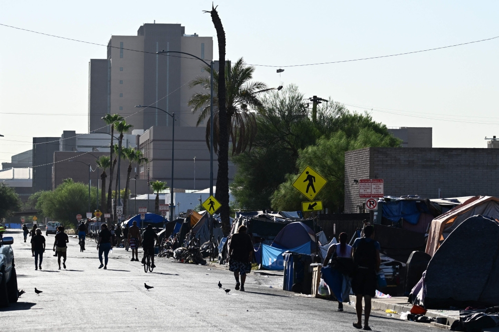 File photo of people walking in the street under the morning sun in ‘The Zone’, a vast homeless encampment where hundreds of people reside, during a record heat wave in Phoenix, wave in Phoenix, Arizona on July 19, 2023. ― AFP pic