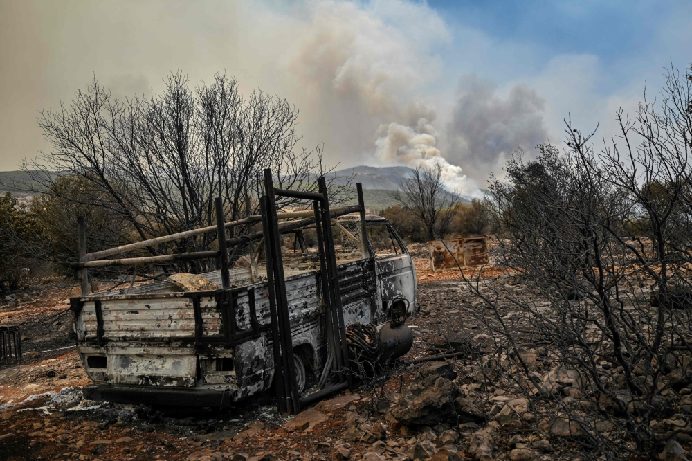 File photo of a burnt out vehicle is pictured as a forest burns in the background in the settlement of Neoi Pontioi, near Athens, on July 19, 2023. ― AFP pic