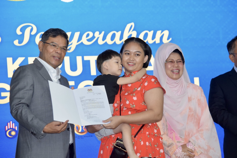 Philip Lai Jung Pah (2nd left) hugs his mother Christina Lendai (2nd right) as by Home Minister Datuk Seri Saifuddin Nasution Ismail hands over the citizenship approval letter, witnessed by Minister of Women, Childhood and Community Wellbeing Development Datuk Seri Fatimah Abdullah. — Borneo Post pic