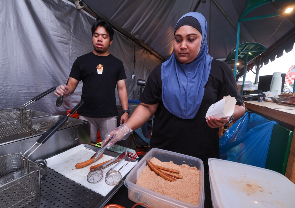 Fifbites Churros sales manager Ima Sallyza Ishak (right) prepares food at her stall at the Kembara Riuh carnival in Fraser Valley July 30, 2023. — Bernama pic
