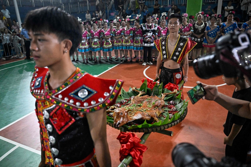 This photo taken early on July 31, 2023 shows performers in Miao ethnic minority costume parading a platter of roast mutton, the prize for the runner-up team. — AFP pic