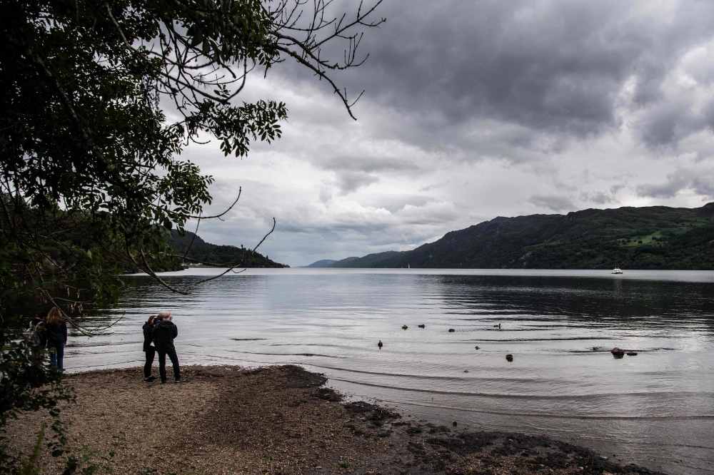 Visitors look at the water of Loch Ness, which is experiencing lower than average water level, on July 6, 2023, in the Scottish Highlands. — AFP pic