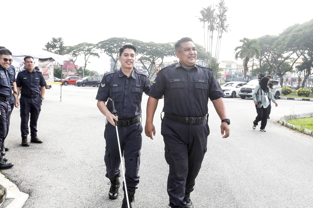 A fellow police officer assists Corporal Abdullah Sidee Mohamed (centre) out of the voting centre at the Kuala Selangor District Police Station August 8, 2023. 
