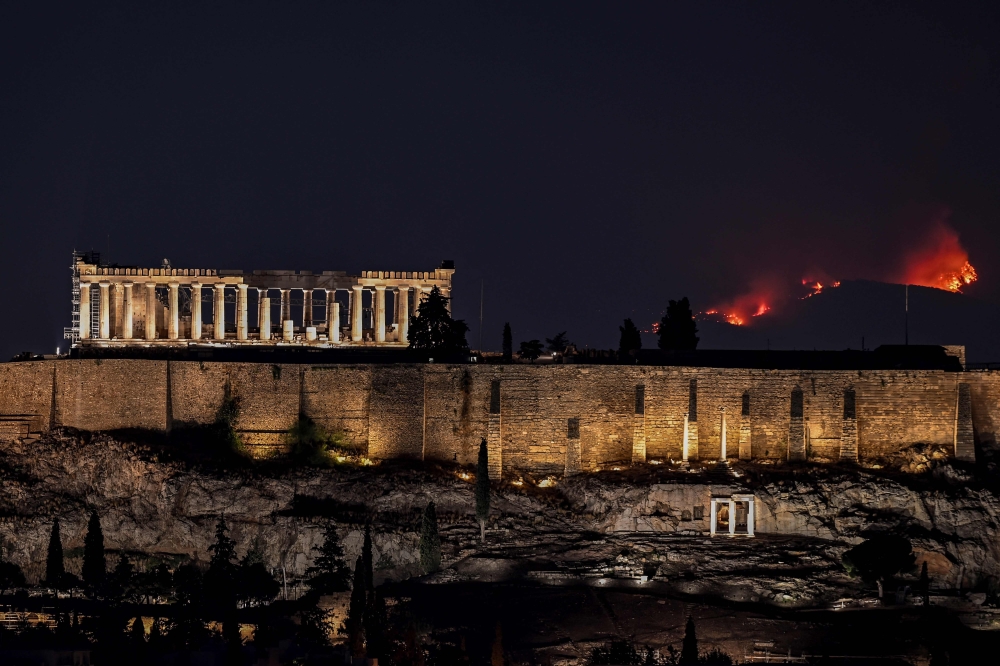 A forest burns behind the Parthenon ancient temple on top of the Acropolis hill as wildfire rages in the outskirts of Athens. — AFP pic