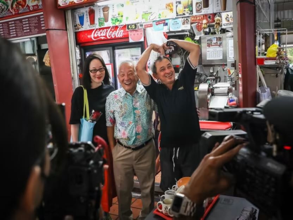 Presidential candidate Ng Kok Song (middle) with his fiancee Sybil Lau, posing for a photo with a stallholder during a walkabout at Ayer Rajah Food Centre on August 29, 2023. — TODAY pic