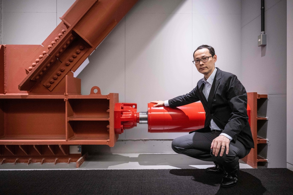 Kai Toyama, a structural engineering official at real estate giant Mori Building, posing for photographs with an oil damper at Toranomon Hills Business Tower in Tokyo. — AFP pic