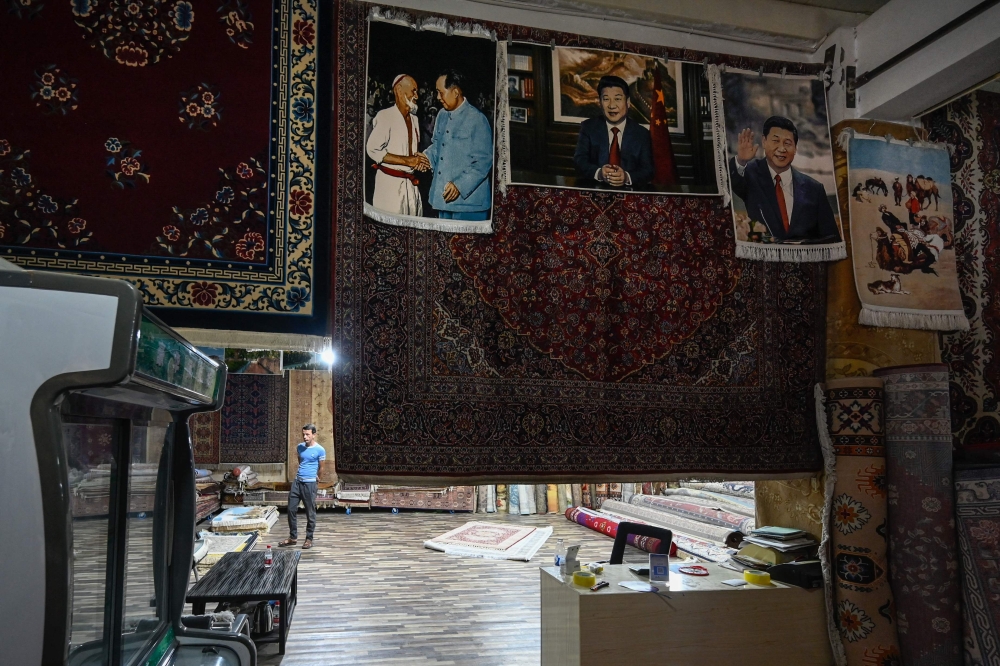 A man in his carpet shop, some with the image of China's President Xi Jinping, in Kashgar city. — AFP pic 