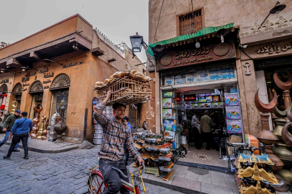 In this picture taken on February 27, 2023, a deliveryman balances a load of bread on his head as he rides a bicycle through a street in the old quarters of Cairo. Annual inflation in Egypt hit 39.7 per cent in August, official figures showed on September 10, an all-time high for the country as it grapples with a punishing economic crisis. — AFP pic