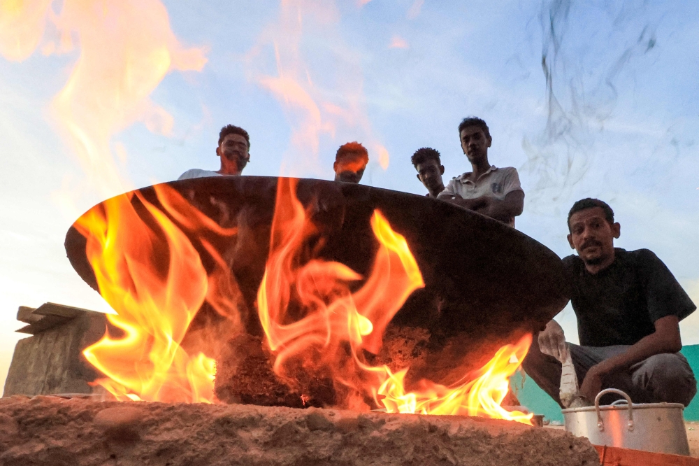 File photo of people sitting around food cooking on a bonfire at a school that has been transformed into a shelter for people displaced by conflict in Sudan’s northern border town of Wadi Halfa near Egypt on September 11, 2023. — AFP pic