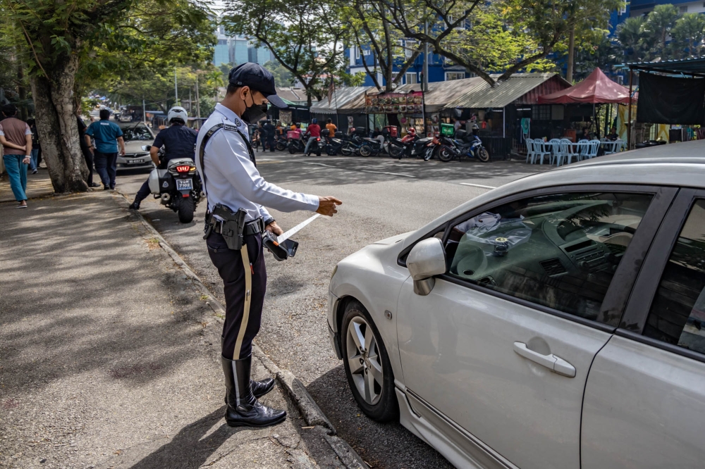 A police officer is seen issuing a summon for an illegally parked car during an operation called ‘Operasi Hormat Undang-undang Jalan Raya’ in Kuala Lumpur in this file photo taken on July 3, 2023. — Picture by Firdaus Latif 