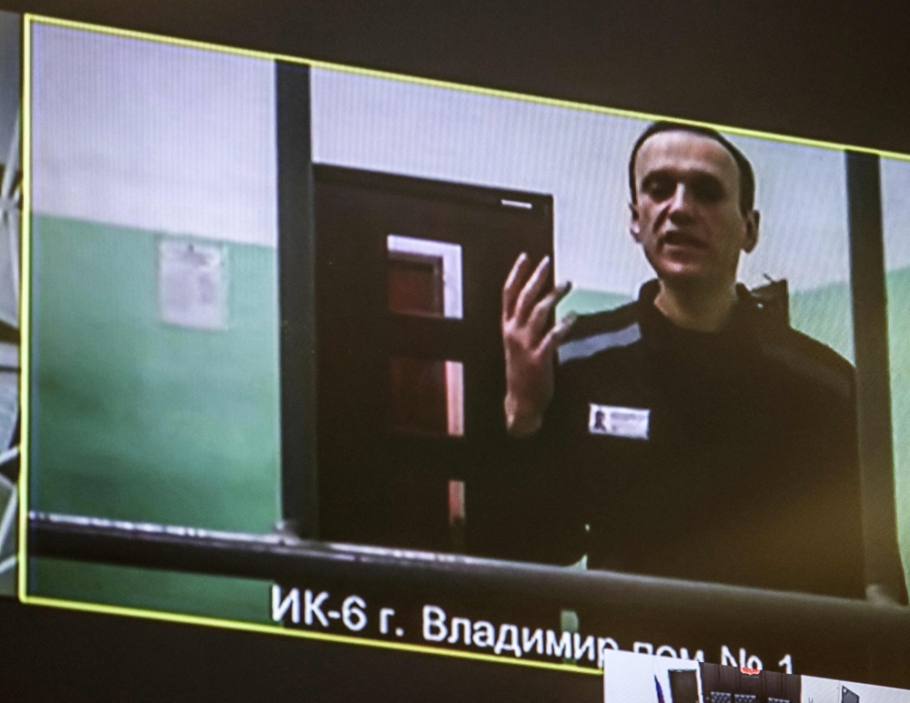 A screen shows jailed Kremlin critic Alexei Navalny as he arrives to listen to a hearing on an appeal lodged against a court decision to jail him for 19 years in a maximum security prison on extremism-linked charges, at a court in Moscow