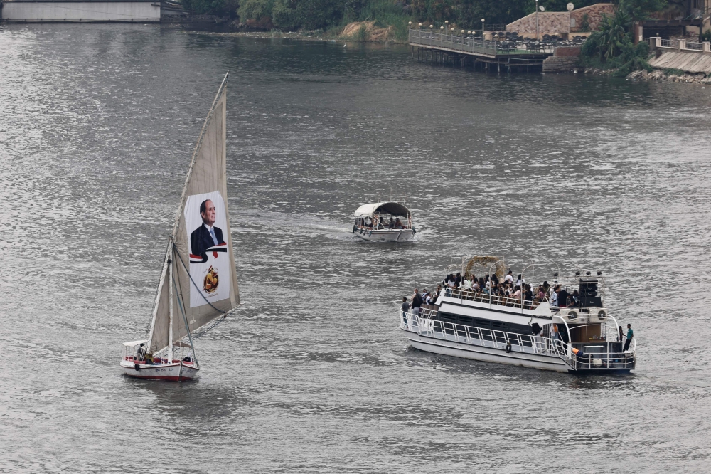 A ferry carries people across the Nile River past a sail boat bearing a portrait of Egypt’s President Abdel Fattah al-Sisi in central Cairo. — AFP pic