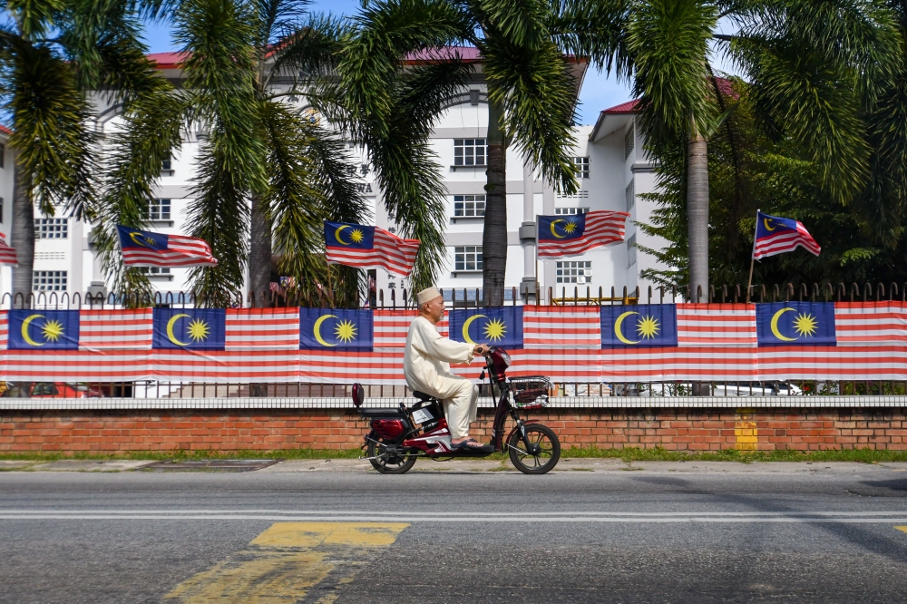 A man on an electric scooter rides past Jalur Gemilang flags in Kota Baru, Kelantan August 17, 2022. — Bernama pic