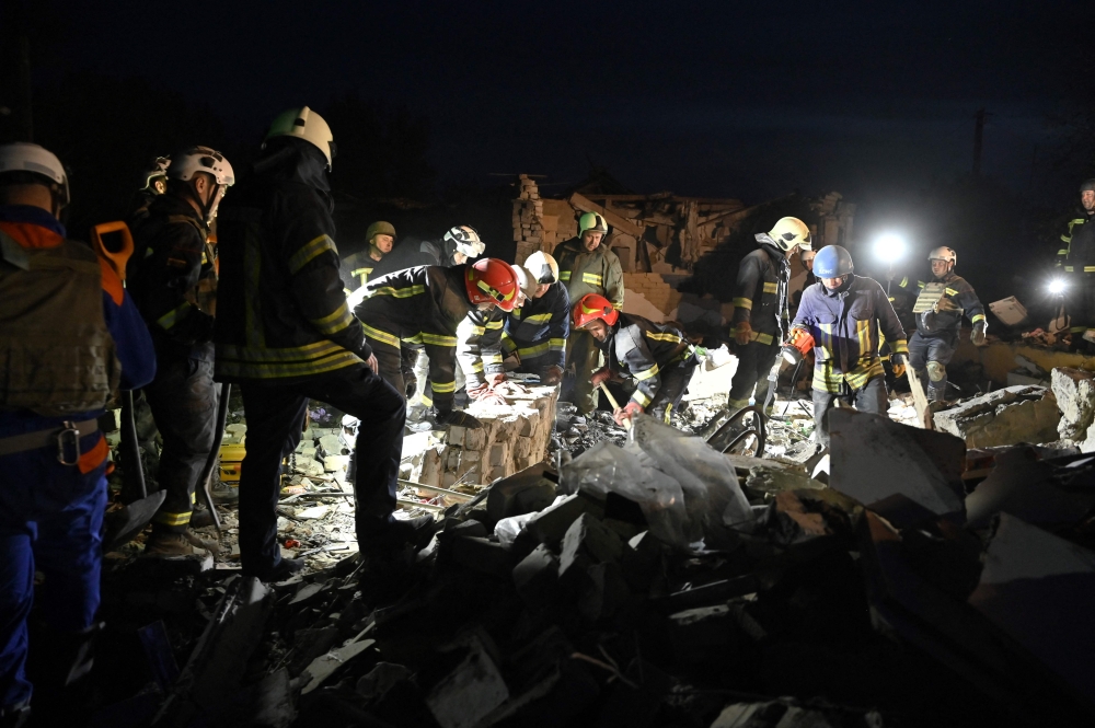 Ukrainian rescuers work amongst rubbles of a destroyed shop and cafe after a Russian strike in the village of Groza. — AFP pic