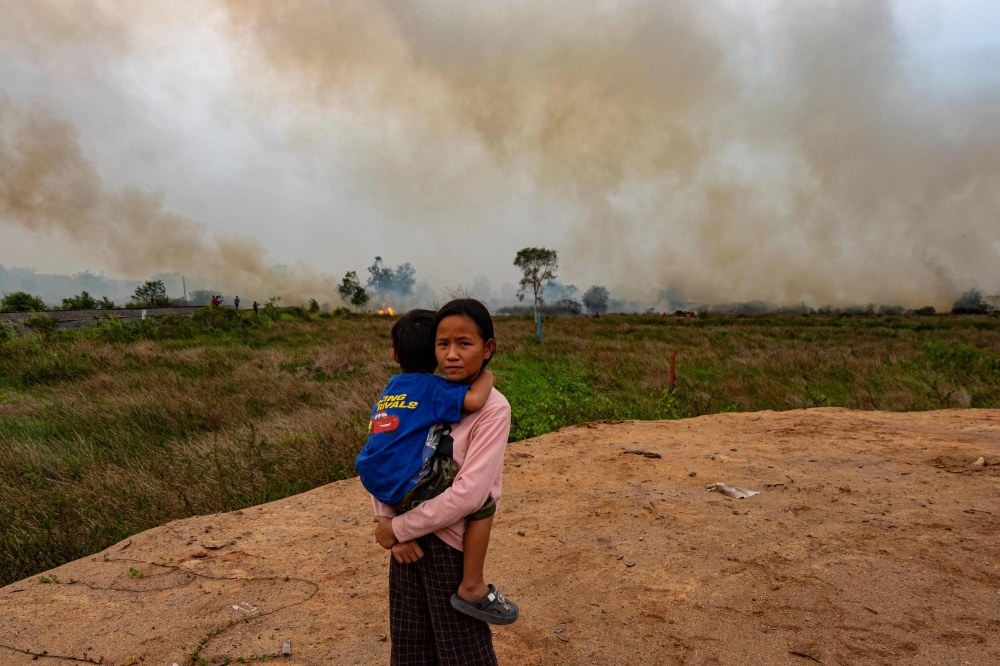 This picture taken on October 4, 2023, shows Poppy, 12, holding her brother as Indonesian firefighters try to extinguish a peatland fire near her house in Palembang, South Sumatra. — AFP pic 