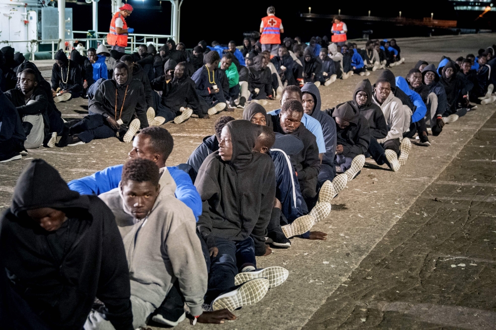Part of a group of 496 migrants sit on the pier following the arrival of the Spanish Civil Guard vessel Rio Segura at the Port of Granadilla, island of Tenerife October 5, 2023. — AFP pic