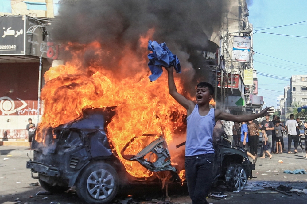 A Palestinian boy next to a burning Israeli vehicle that Palestinian gunmen brought to Gaza. — Reuters pic