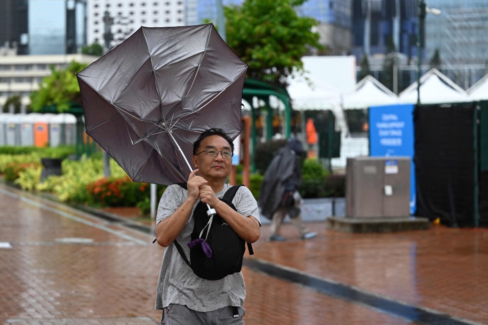 A man has his umbrella turned inside out as Hong Kong hoisted typhoon signal no 8 around noon on October 8, 2023 as typhoon Koinu skirted by after the financial hub was affected again by a super typhoon and historic rainstorm last month. — AFP pic