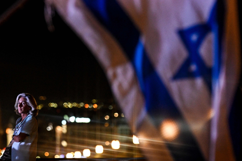 A woman stands next to Israeli flag as she takes part in a vigil for the Israeli victims at Eduardo VII park in Lisbon on October 10, 2023. — AFP pic
