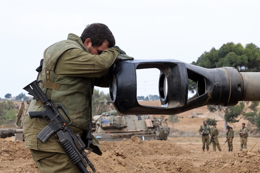 An Israeli soldier rests his head on an artillery gun barrel of an armoured vehicle as Israeli soldiers take positions near the border with Gaza in southern Israel on October 9, 2023. — AFP pic