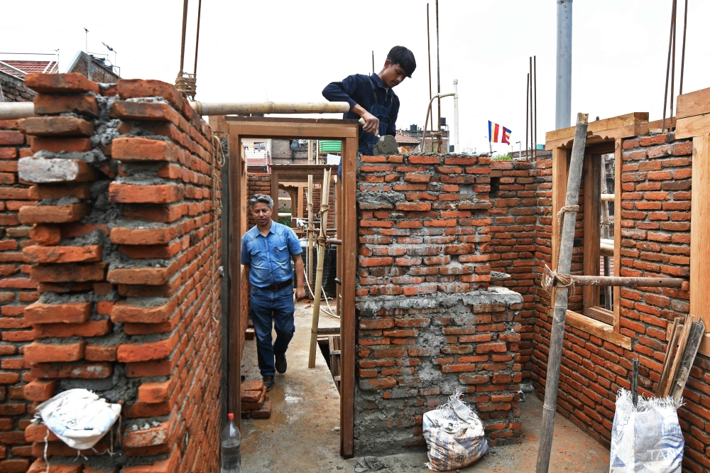 In this photograph taken on June 14, 2023, heritage conservationist and Nepal Vocational Academy founder Rabindra Puri (L) walks past a labourer working to reconstruct a temple in Bhaktapur on the outskirts of Kathmandu. — AFP pic