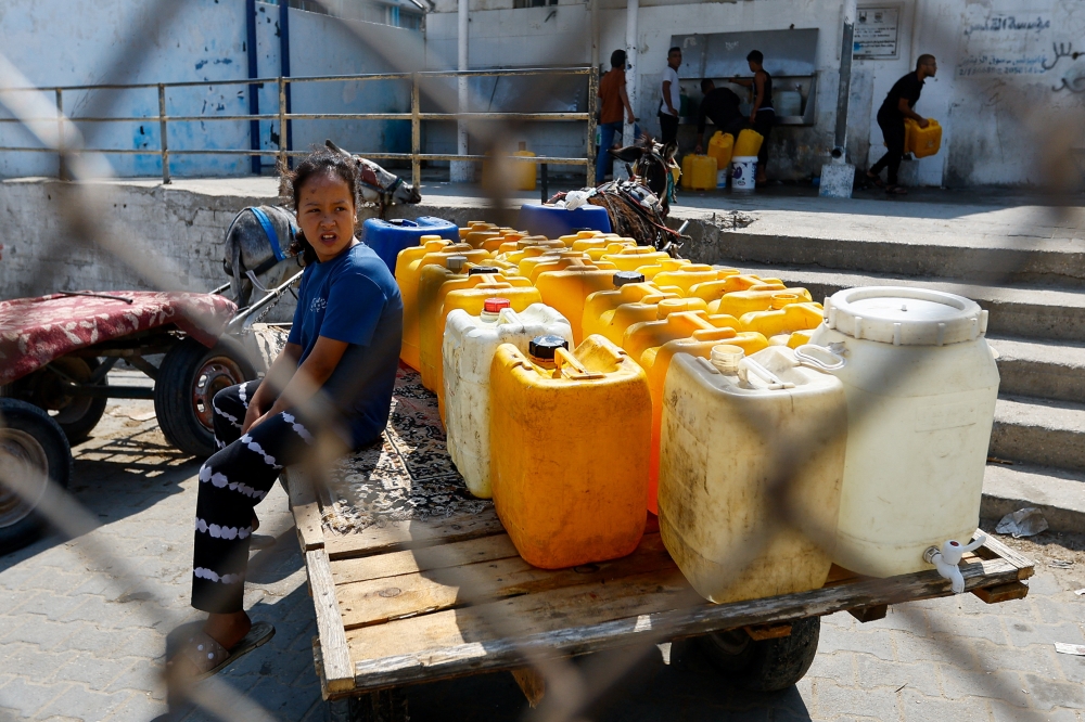 A girl sits next to containers as Palestinians gather to fill water from public taps amid the conflict with Israel in Khan Younis, in the southern Gaza Strip. — Reuters pic