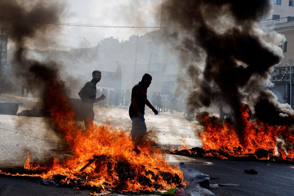 People walk next to fires as Palestinians take part in a protest following Israeli strikes on Gaza, in Nablus, in the Israeli-occupied West Bank October 13, 2023. ― Reuters pic