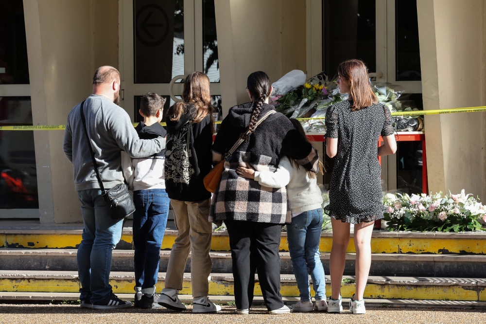 People stand in attention before flowers layed in front of the Gambetta high school in Arras, north-eastern France on October 14, 2023, the day after a teacher was killed and two other people severely wounded in a knife attack. — AFP pic