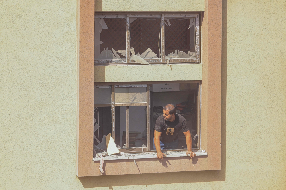 A Palestinian man looks through the window of a damaged building after Israeli strikes, in Khan Yunis in the southern Gaza Strip on October 14, 2023. — AFP pic